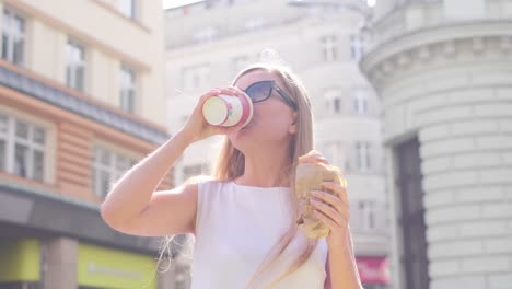 vertical video beautiful girl eats a donut and drinks coffee standing against the background of a