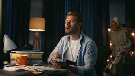 focused man writing remarks at home closeup. woman dancing vacuuming at evening