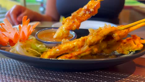 sumergir palitos satay de pollo tradicionales en salsa de cacahuete en un restaurante tailandés, comida tailandesa sabrosa, toma de 4k
