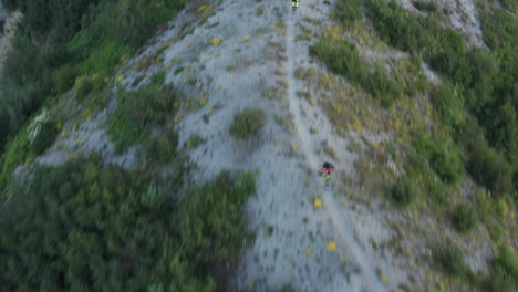 extreme downhill mountainbiking going down gravel trail on mountain ridge, aerial