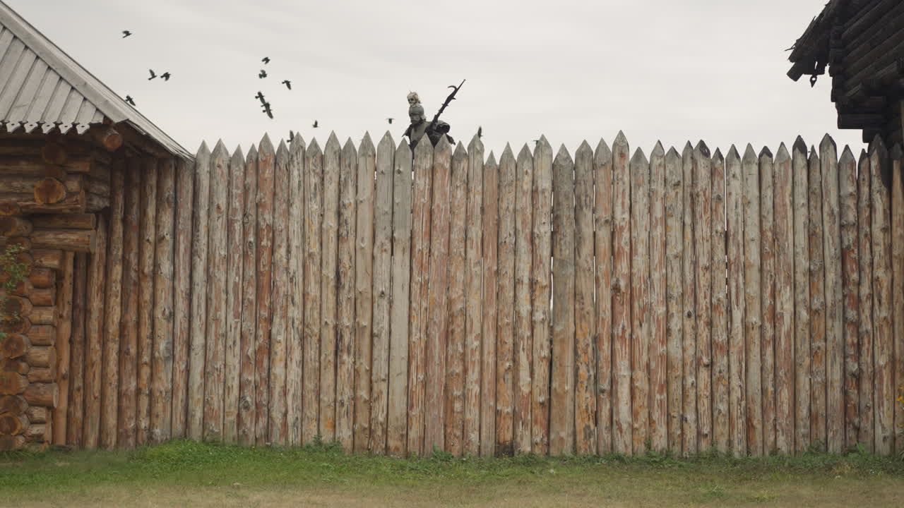 человек в доспехах идет по платформе возле высокого бревенчатого заграждения