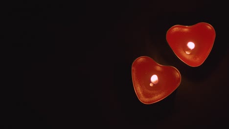 close up of two romantic lit heart shaped red candles on black background with copy space