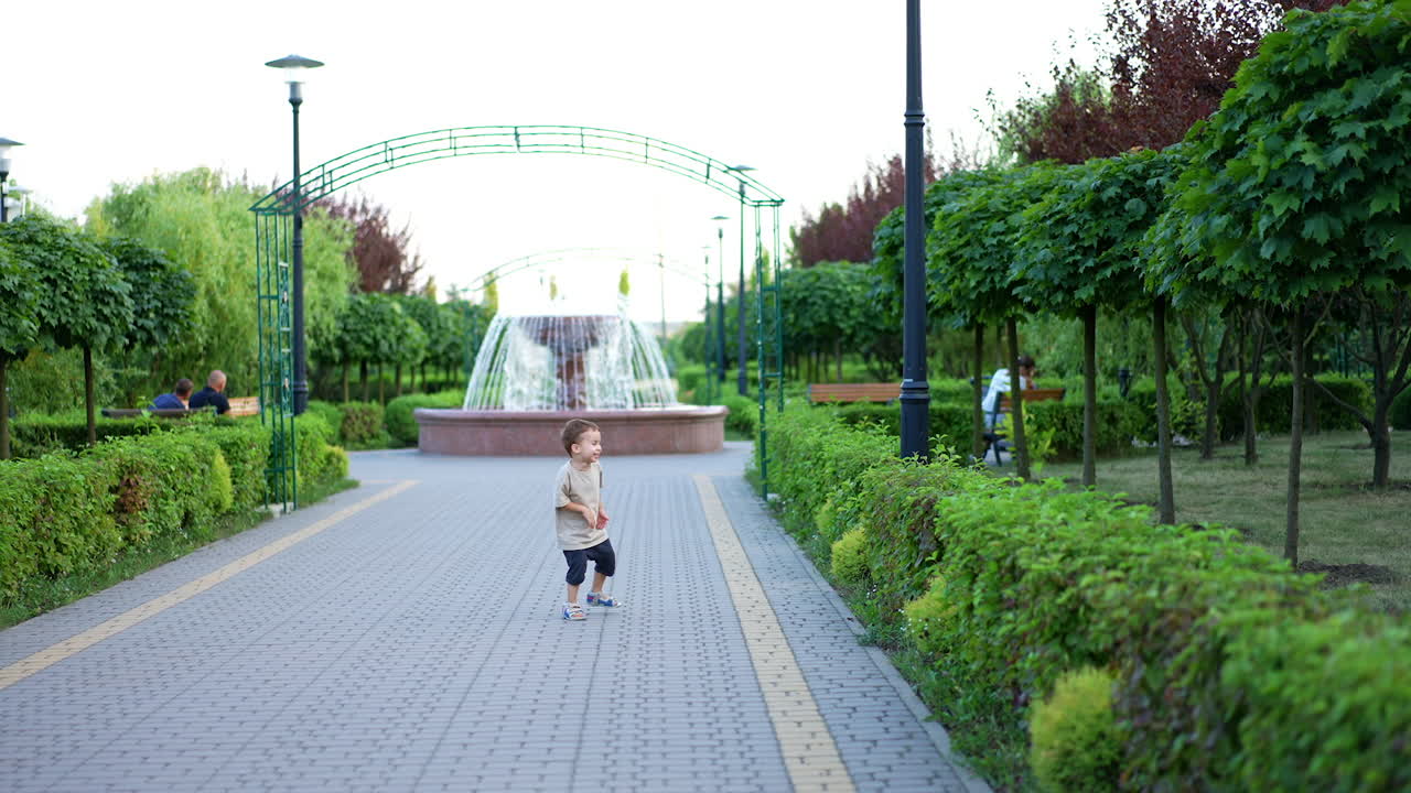 Adorable Caucasian kid running happily by the park. Joyful baby boy stops, looks at camera and continues to run.