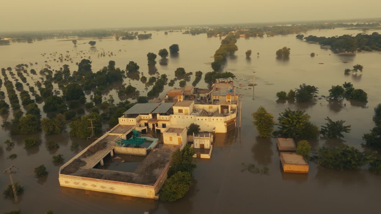 Aerial video over large residential complex surrounded by flood waters and submerged trees under an intense orange afternoon sun