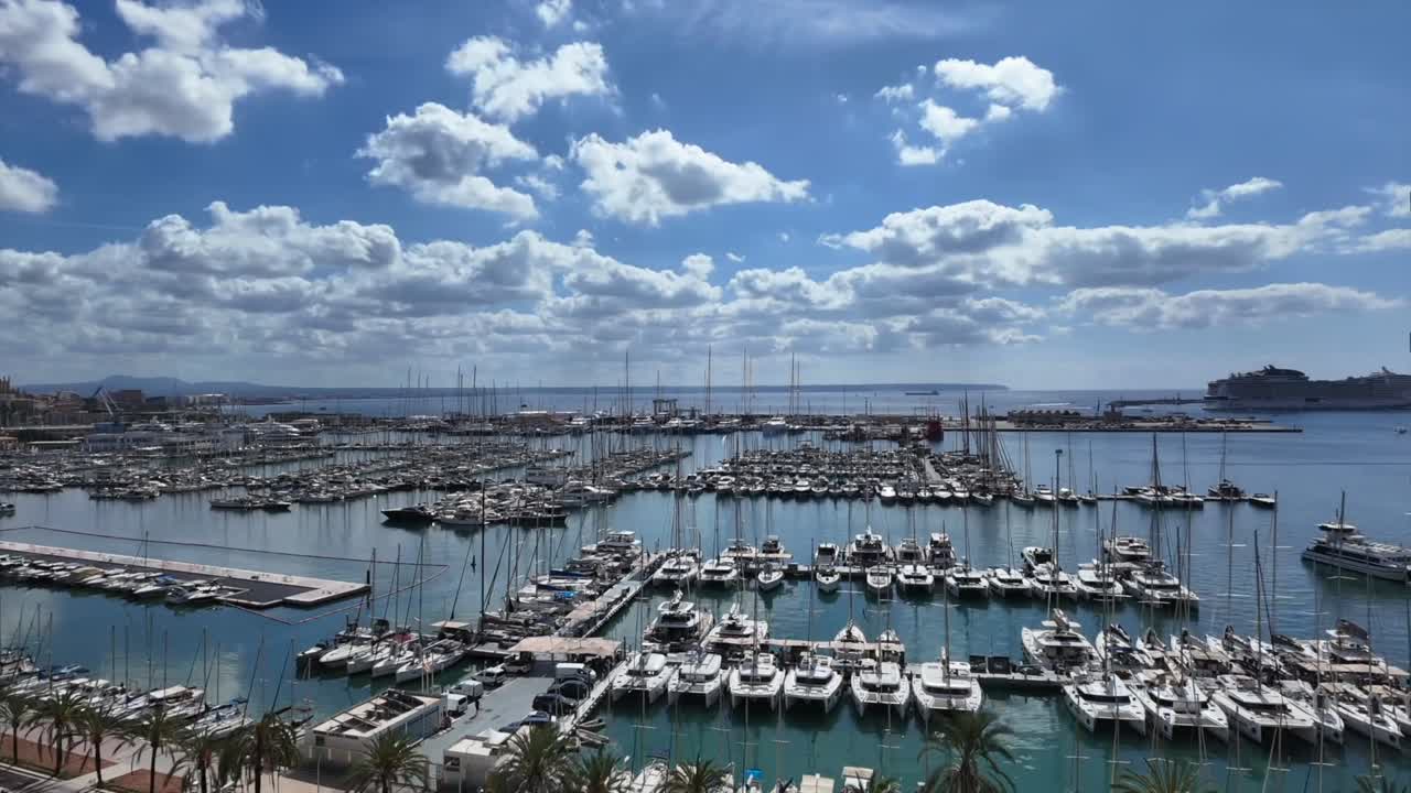 An elevated perspective of Palma de Mallorca Marina with boats coming and going and moving scattered clouds in a blue sky