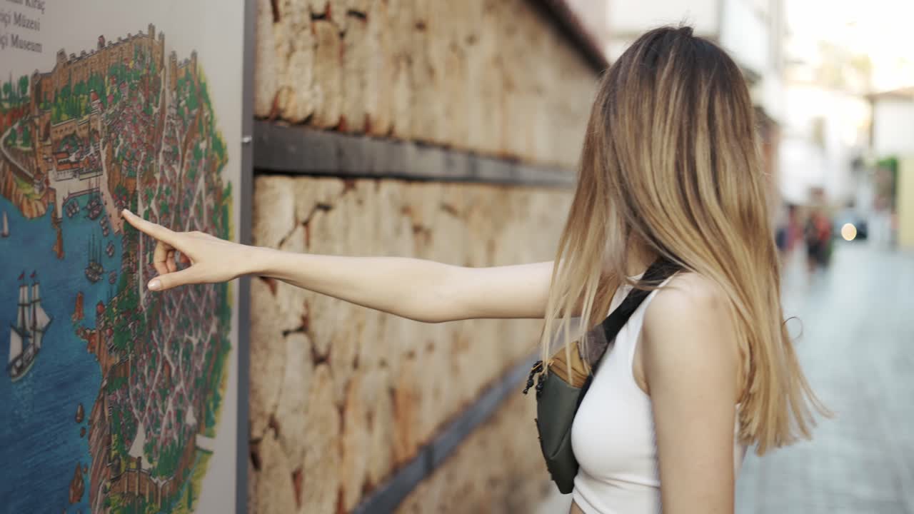 벽 지도로 서있는 금발 여성 관광객, 손가락을 가리키는