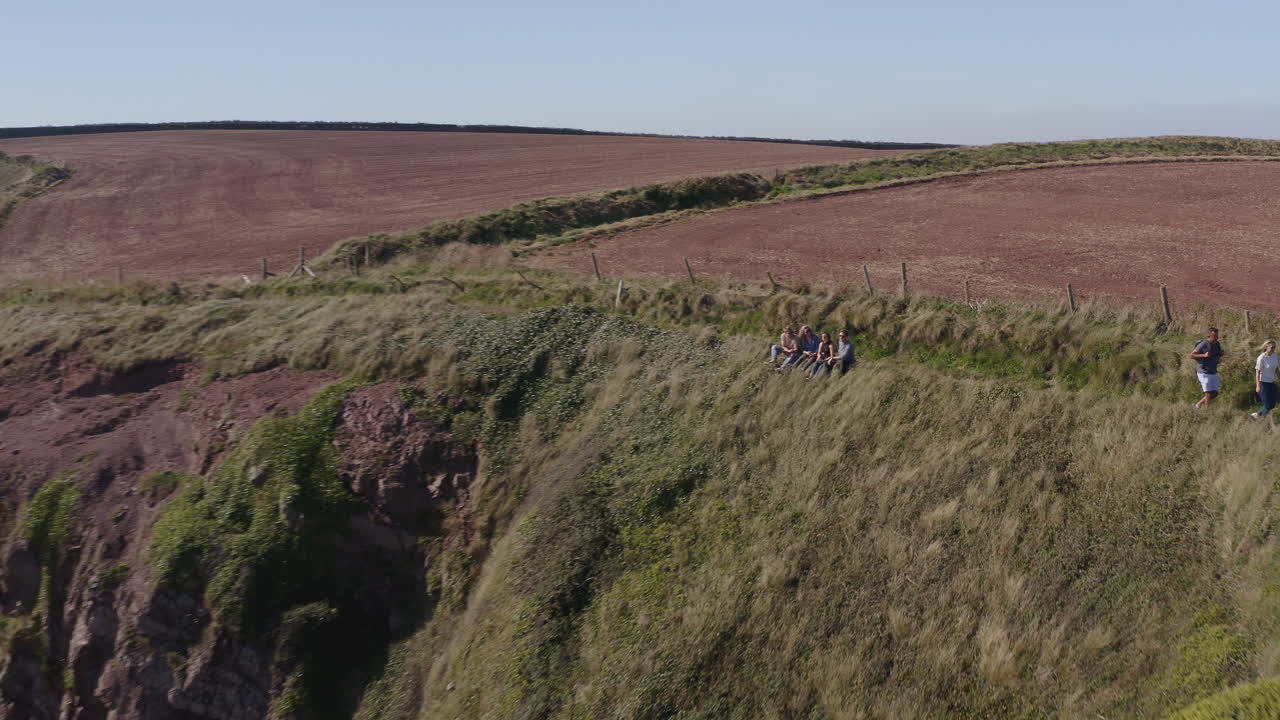 снимка с дроном группы друзей, делающих селфи, когда они прогуливаются по скалам на прибрежной тропе