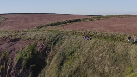 Drohnenaufnahme-Einer-Gruppe-Von-Freunden,-Die-Ein-Selfie-Machen,-Während-Sie-Auf-Dem-Küstenweg-Entlang-Der-Klippen-Wandern