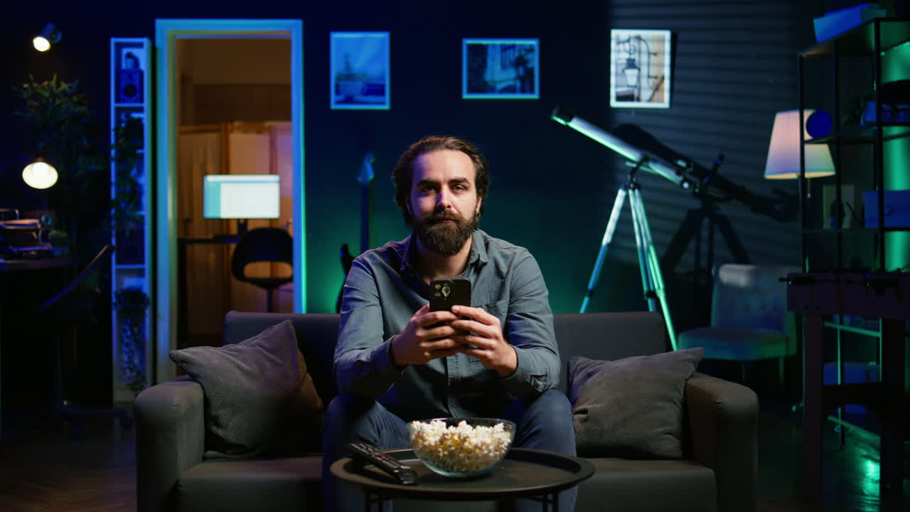 집에서 소파에서 휴식을 취하고 스마트폰으로 친구들에게 문자 메시지를 보내는 남자