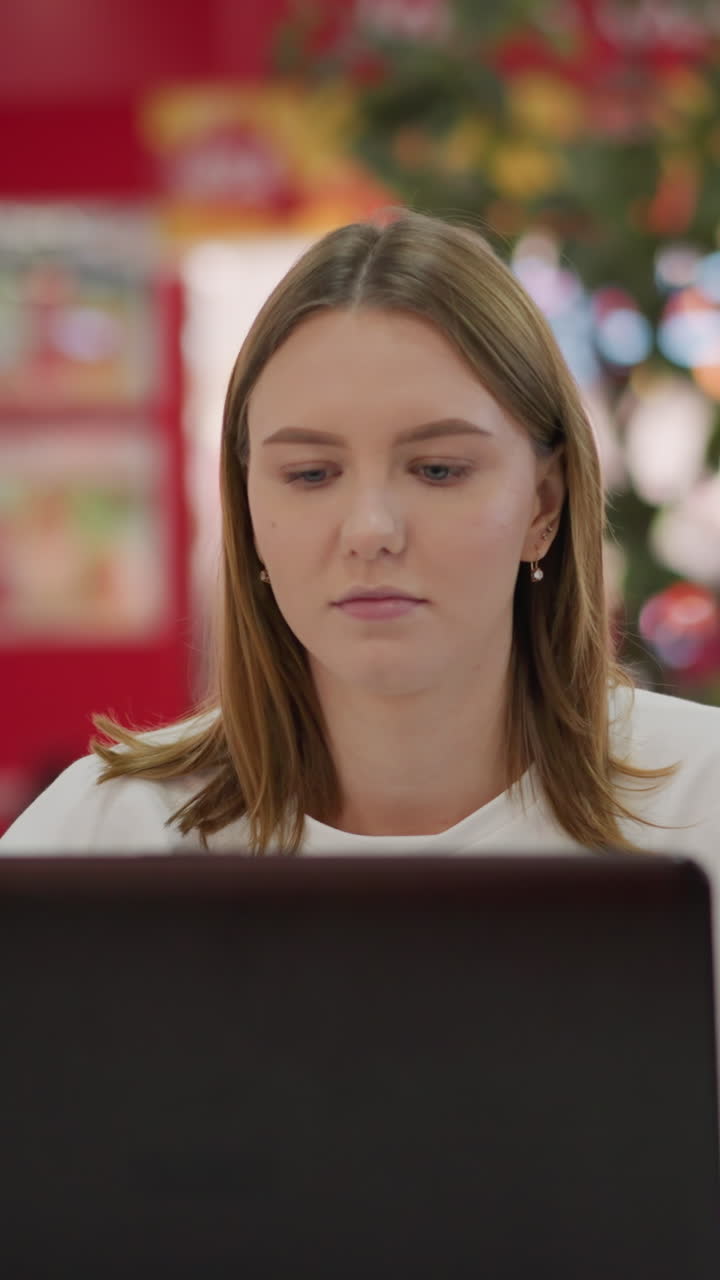 freelancer trabajando en una computadora portátil en el patio de comidas, escribiendo y concentrándose, sentado en una mesa en el interior de un centro comercial moderno con colores vibrantes, señalización de marca y actividad borrosa en el fondo
