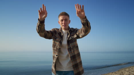 Positive-guy-say-hello-on-camera-relaxing-on-beach.-Handsome-tourist-run-vlog.