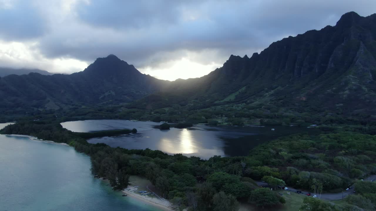 toma aérea de la bahía de kaneohe y el estanque de peces molii mientras el sol se pone detrás de un espectacular telón de fondo de montaña en un paraíso tropical