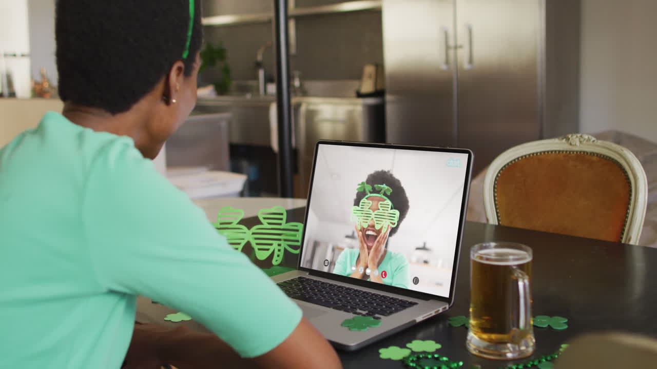 Donna afroamericana sorridente che indossa oggetti a forma di trifoglio in videochiamata sul laptop