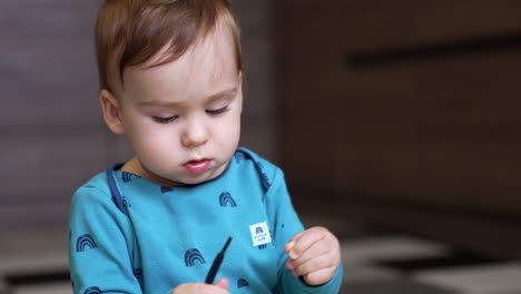 focused toddler looking at the black cord in his hands. lovely child in blue shirt playing with a shoe lace. close up. blurred backdrop.