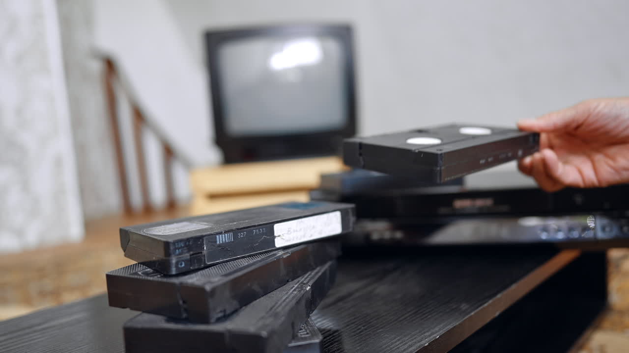 Pile of old VHS cassettes on the table. Male places some tapes on the recorder and puts one into the player