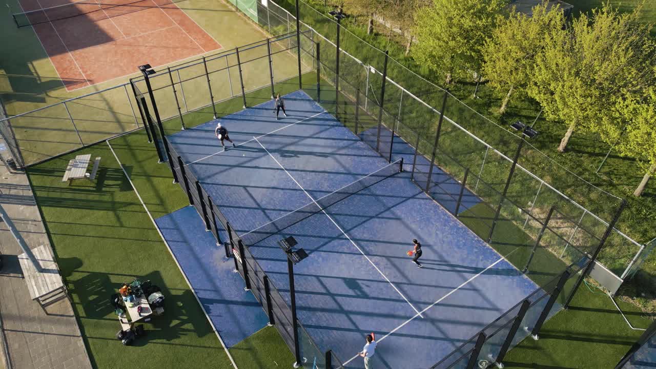 Aerial footage of a padel sports complex featuring multiple courts in action, surrounded by trees and recreational areas.