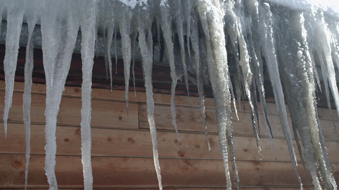 Icicles Hanging From Wooden Eaves On Sunlit Cabin Roof, Long Translucent Spikes Slowly Dripping Water, . Media