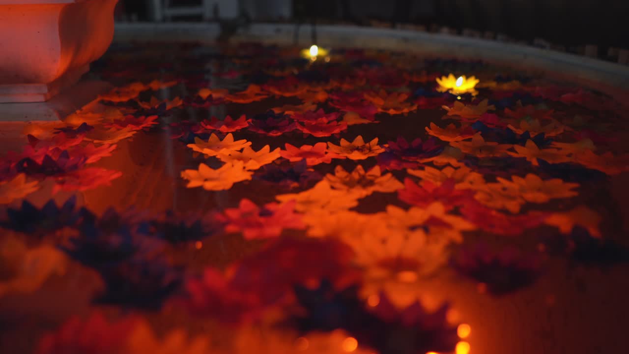 Colorful flowers and candles rotating in a pool under dim light from a different angle.Such a tranquil scenery.