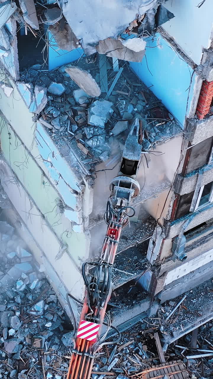 Demolishing vehicle breaks and throws down the parts of ruined house. Dismantling the old building with the help of machinery. View from above. Vertical video