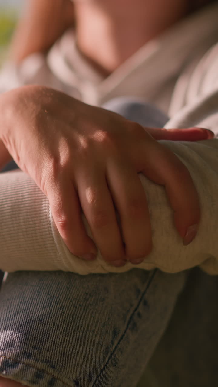 primer plano de los brazos de una mujer joven doblados sobre las rodillas, las manos descansando suavemente, con la luz del sol proyectando reflejos suaves, vestimenta casual con fondo natural borroso