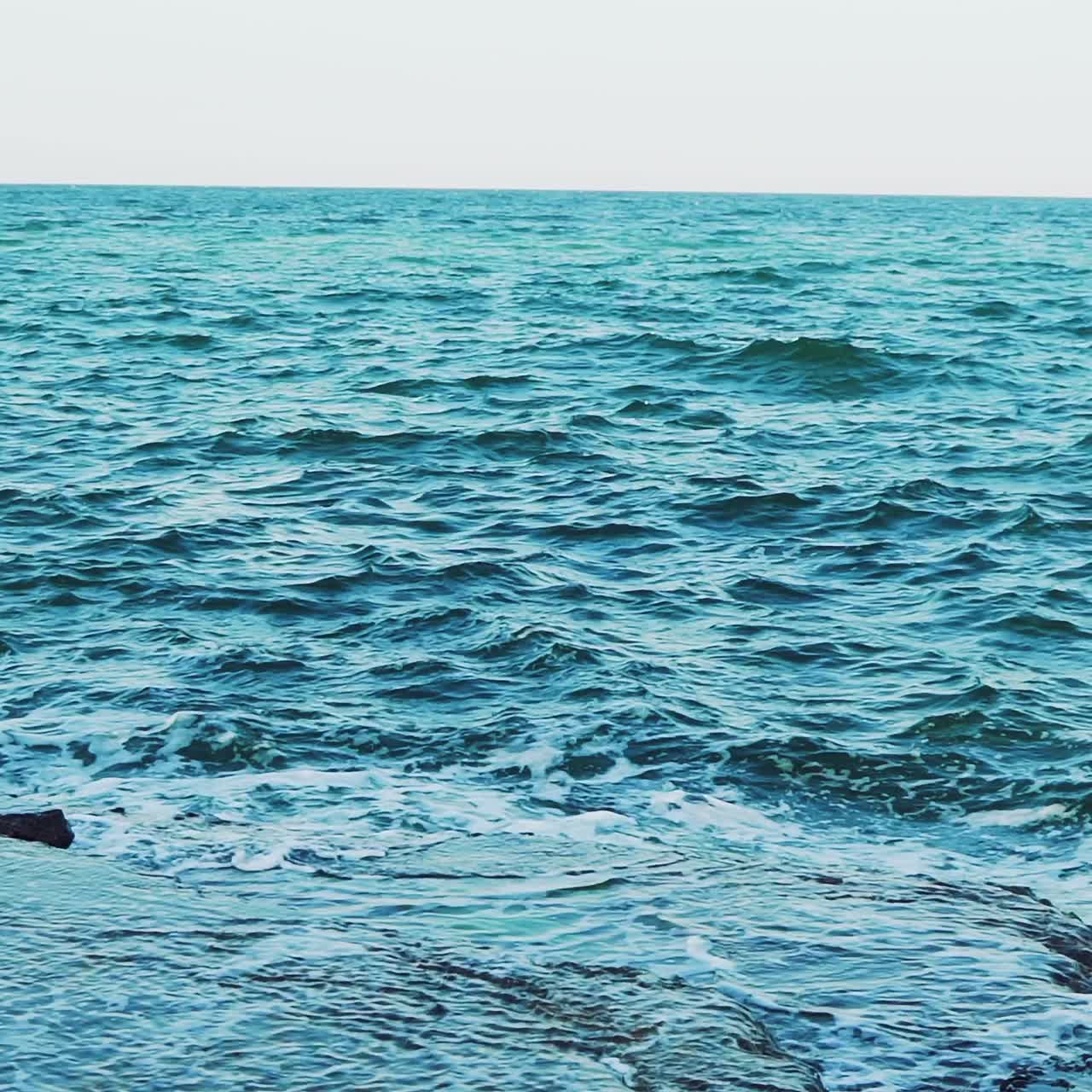 Crests of the waves are breaking on the reefs near the shore in the summer. Seascape. Slow motion. Aerial view