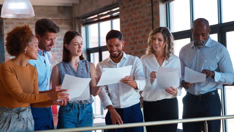 Smiling-Multi-Cultural-Business-Team-Standing-Together-Meeting-Discussing-Paperwork-In-Modern-Office