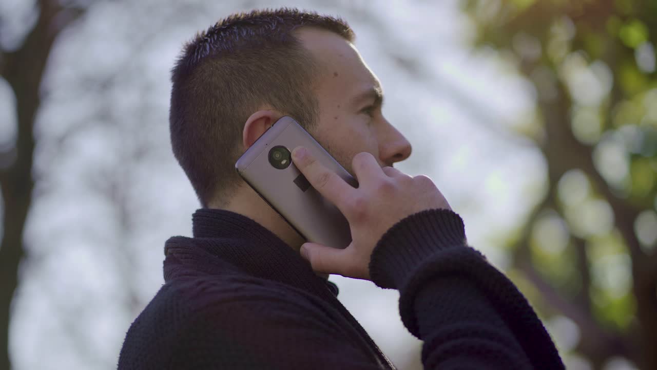 joven teniendo una conversación a través de un teléfono moderno al aire libre