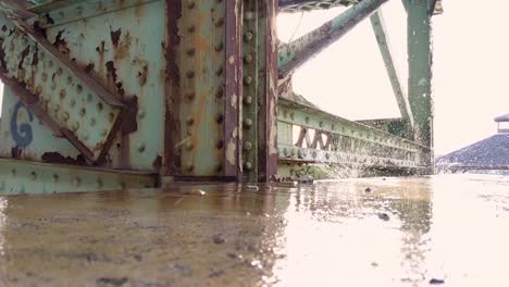 Slow-motion-rain-drops-from-rusty-abandoned-bridge-onto-concrete