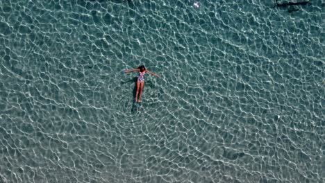 aerial top view over a woman relaxing and enjoying crystal clear waters, paros