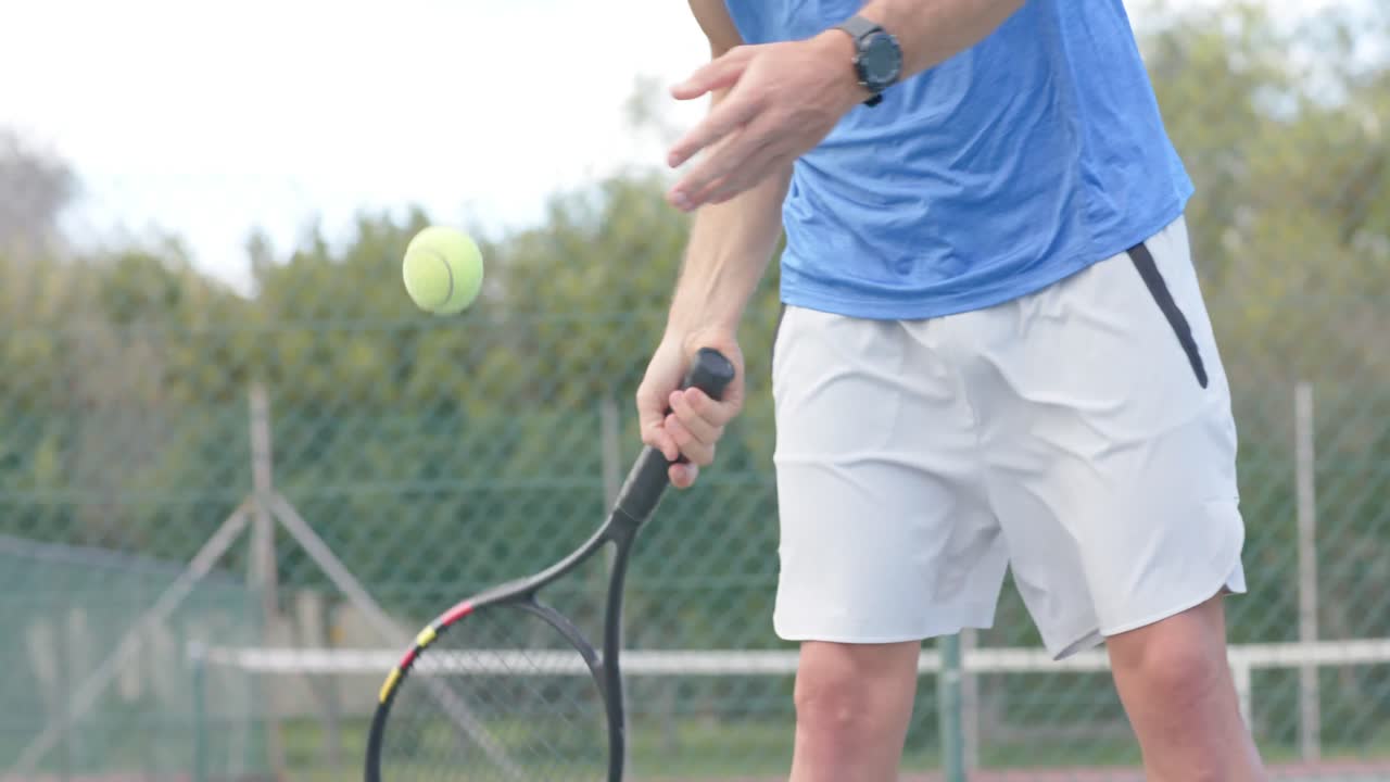 Midtseksjon av kaukasisk mannlig tennisspiller som slår ballen med racket på utendørsbane i sakte film