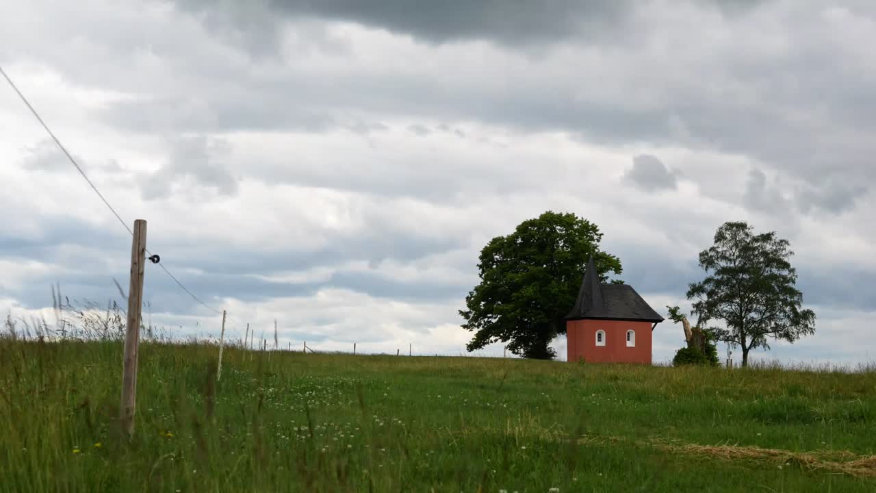 lapso de tiempo de un prado en friesenhagen alemania con la capilla de st anna y dos árboles en la distancia bajo las nubes que pasan en el cielo