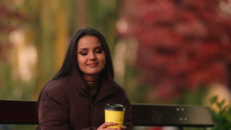 Beautiful-young-woman-with-her-eyes-closed-and-a-dreamy-smile,-enjoying-her-morning-coffee-in-a-park