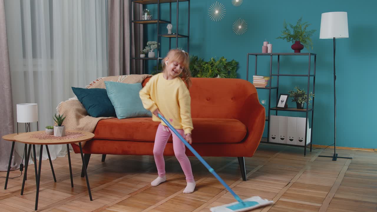 Child girl kid washes floors with a mop in domestic living room dancing singing in positive mood