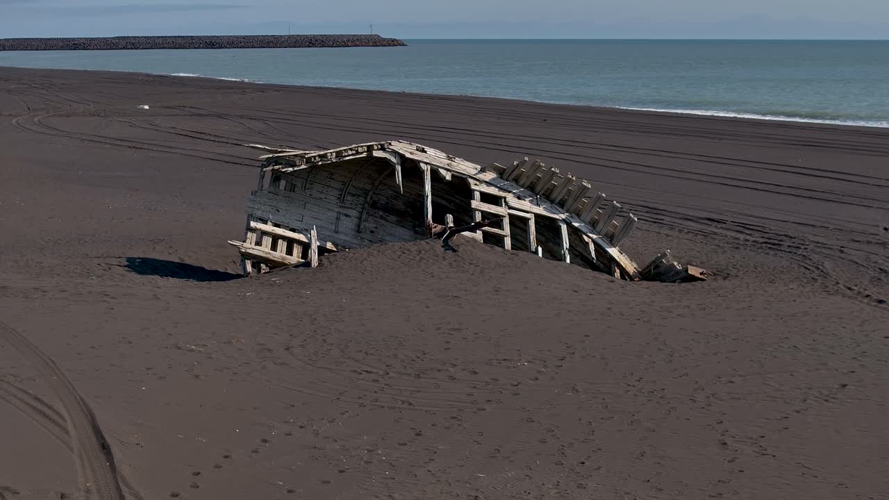 Remains Of A Wooden Shipwreck Partially Buried In The Black Sand Beach In Vestmannaeyjar, Iceland. - aerial ascend shot