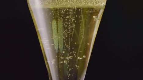 Luxury bubbles are dancing in a champagne glass in elegant dark background. Slow motion