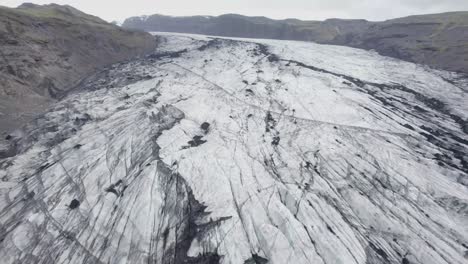 aerial view over darkened, sooty glacier surface, in iceland - reverse, drone shot