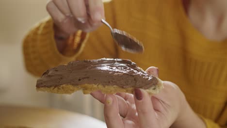 Junges-Mädchen,-Das-Mit-Einem-Löffel-Schokoladenaufstrich-Auf-Ein-Brot-Legt