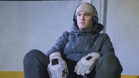 atleta sentado en el suelo con guantes y auriculares, relajándose después de la sesión de entrenamiento bajo una iluminación brillante, expresión tranquila y postura casual reflejan enfoque y determinación