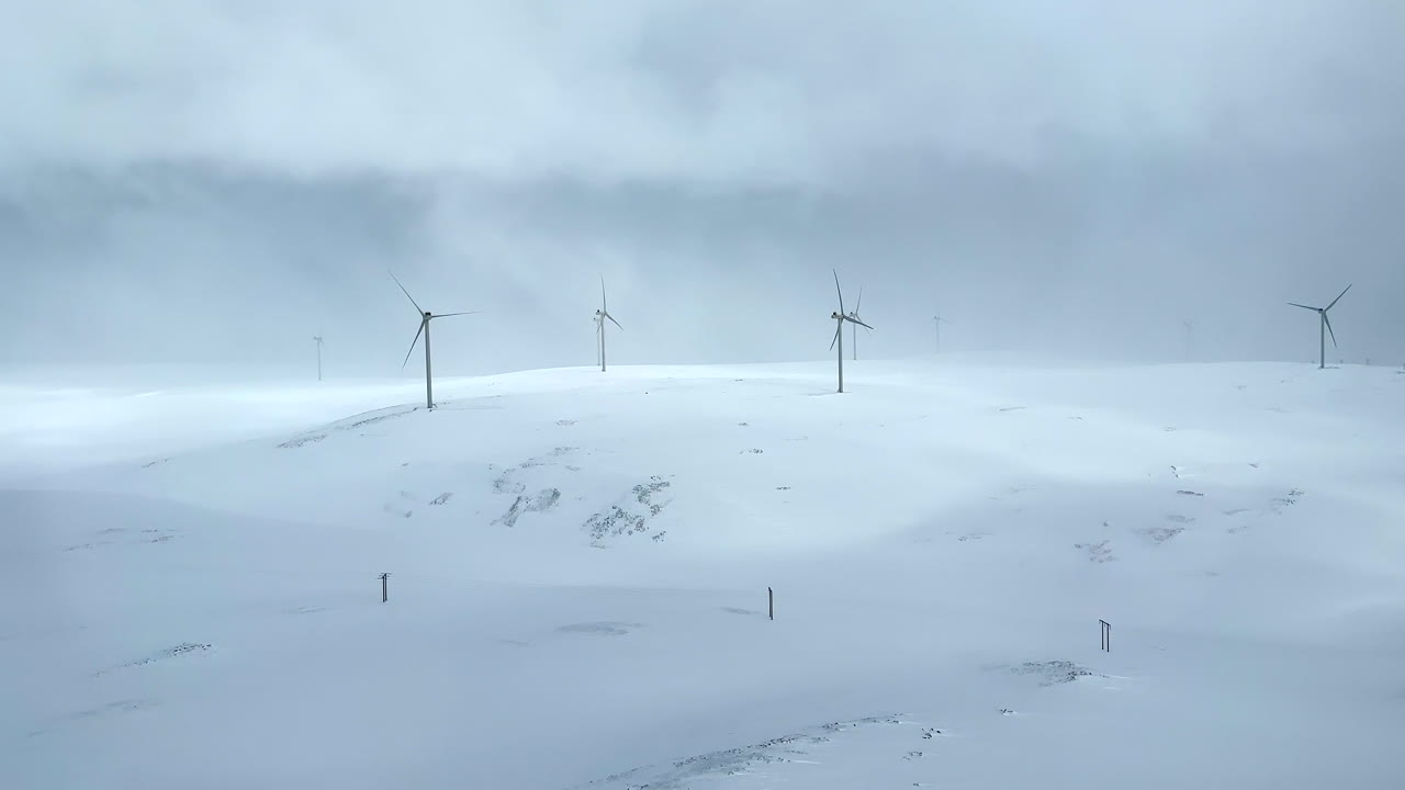 panoramic handheld aerial view of a wind farm in a snow storm in northern norway с ветряными турбинами, вращающимися на холмистом зимнем ландшафте в снежной буре