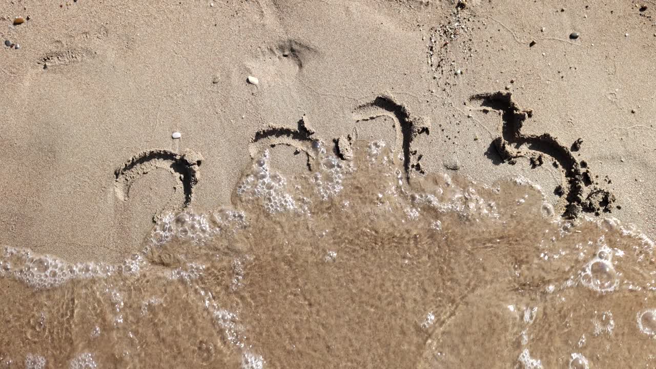 I numeri 2023 disegnati sulla sabbia vengono spazzati via da un'onda del mare