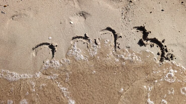 I numeri 2023 disegnati sulla sabbia vengono spazzati via da un'onda del mare
