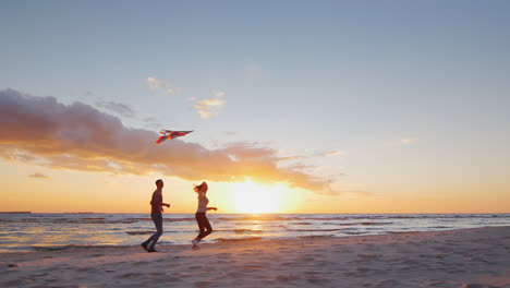 Junges-Paar-Spielt-Mit-Einem-Drachen-Am-Strand-Bei-Sonnenuntergang