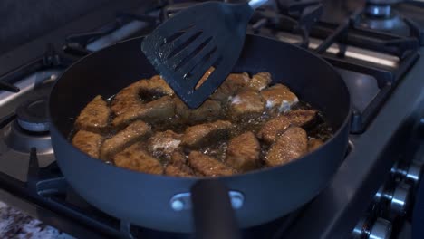 plastic slotted turner being used sizzling frying pan to check on salmon pieces