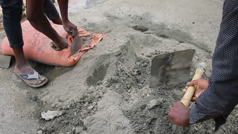 two mason workers unloading cement powder from a bag and working with shovels on the ground in bangalore, india