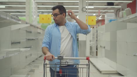 cliente masculino confundido y desconcertado en una tienda contra el fondo de estanterías vacías