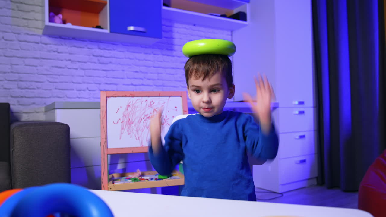 Smiling Caucasian toddler disassembles a big toy pyramid on the desk. Lovely baby puts toy details on his head.