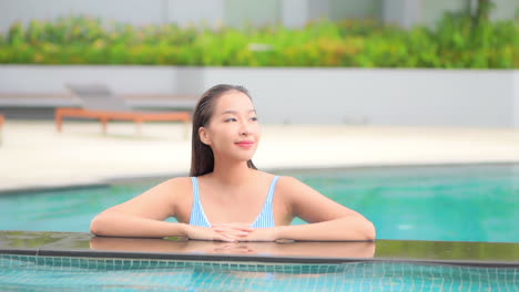 Joven-Y-Atractiva-Mujer-Asiática-Apoyada-En-El-Borde-De-La-Piscina-Disfrutando-De-Sus-Vacaciones-Tropicales