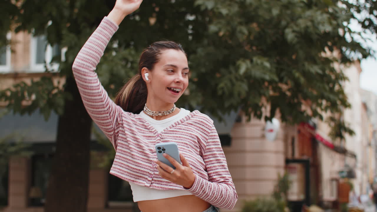feliz mujer relajada de pie en la calle de la ciudad en auriculares inalámbricos escuchando música de baile al aire libre