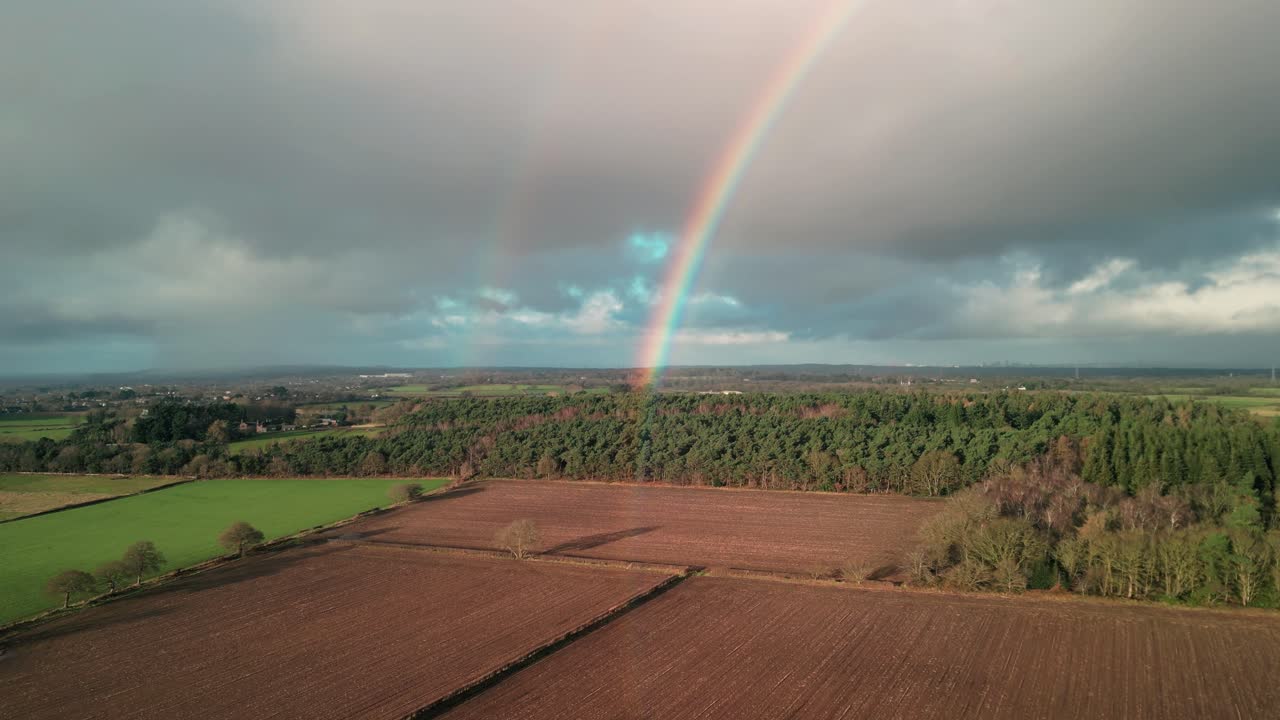 Wintertime sunny aerial drone flyover towards a beautiful double rainbow over the Cheshire countryside, UK