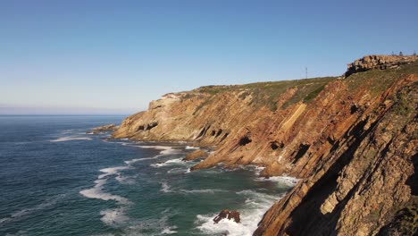 disparo de un dron volando al lado de un enorme acantilado junto a las olas del océano rompiendo contra él